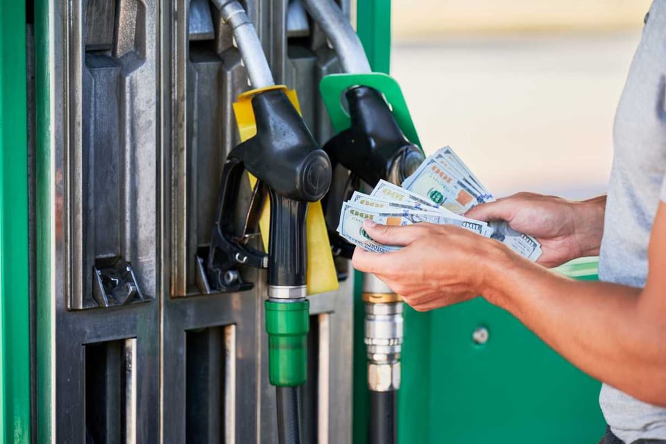 persona contando billetes frente al surtidor de gasolina