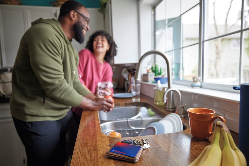 Young African-American man and young mixed-race woman in kitchen doing the dishes Tarjeta de crédito myWalgreens®