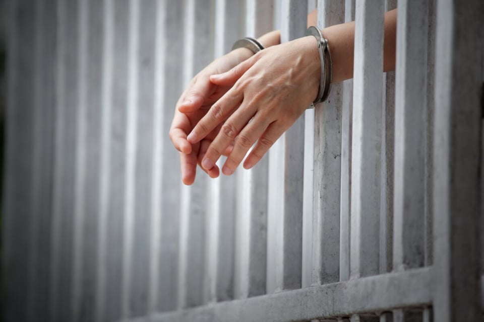 Hands with handcuffs on jail bars