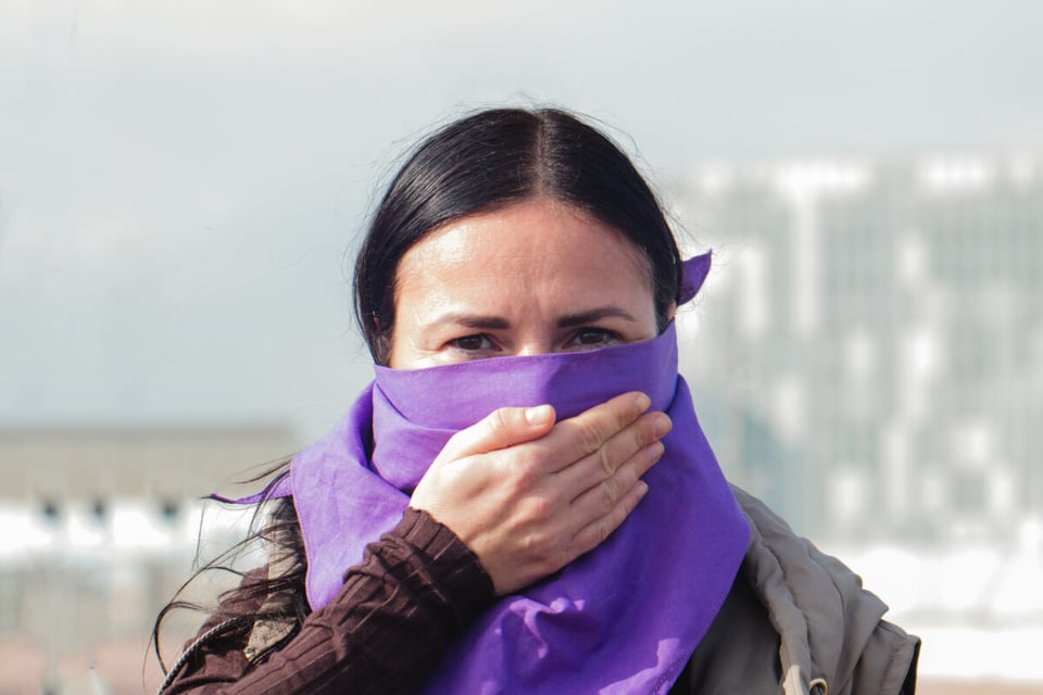 Mujer con trapo morado cubriendo su boca como símbolo de protesta contra el feminicidio