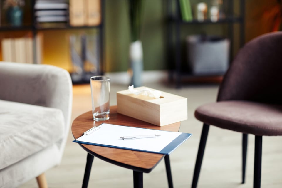 Psychologist's office desk with a glass, tissues, and writing pad.