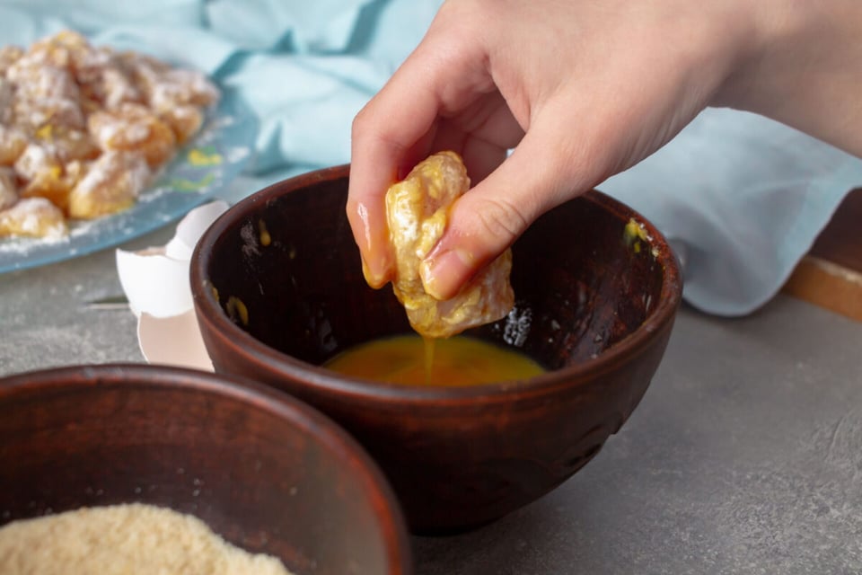 Mano remojando nuggets en huevo