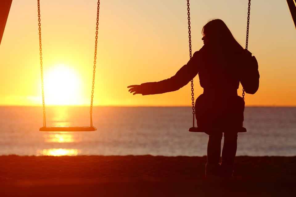 Sunset with a woman in swings with one empty as an idea of disappearance