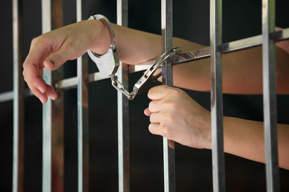 Manos de mujer con esposas en unas barras de celda