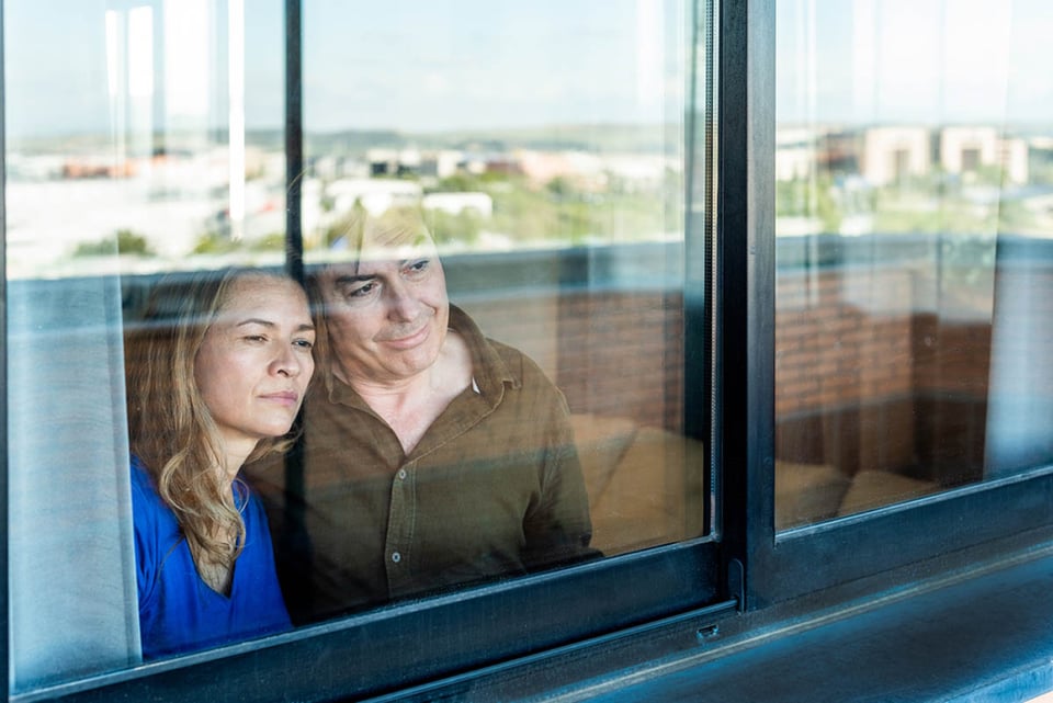 Mature couple, looking out the window, home.