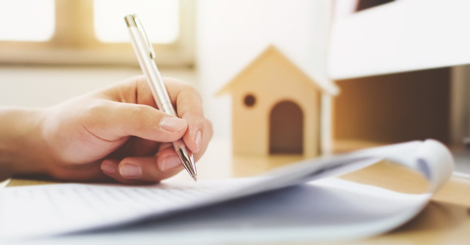 Una casa de madera junto con un contrato siendo firmado