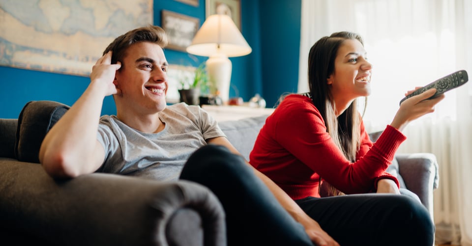 Un hombre junto con una mujer mirando estrenos en televisión