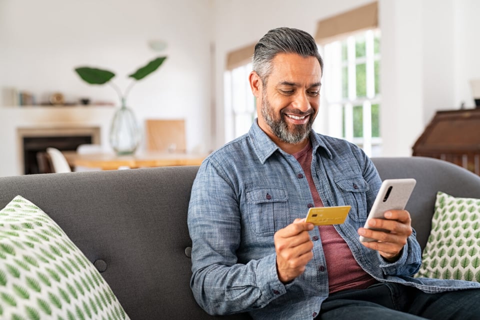 hombre con tarjeta de crédito, hombre con celular, hombre sentado en un sofá, Economía, MundoNOW