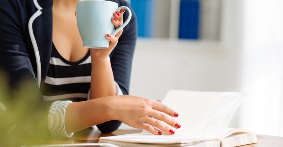 Una trabajadora con café junto con un libro que lee