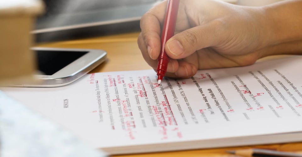 Una persona haciendo anotaciones en ensayos de estudiantes