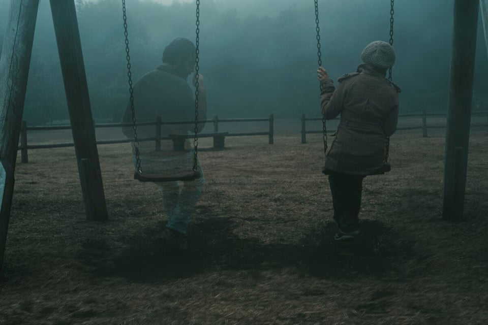 Columpios con una persona transparente y otra entera en medio del fenómeno neblina