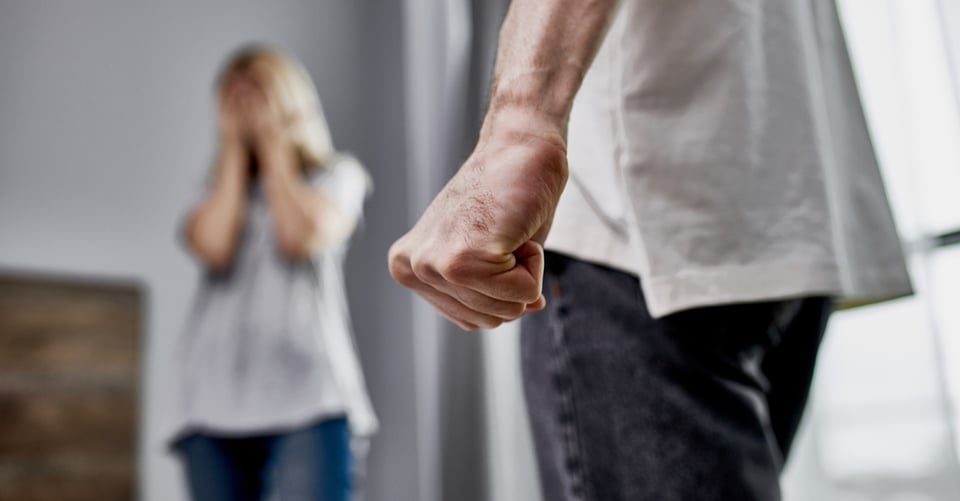Man with clenched fist near woman covering her face