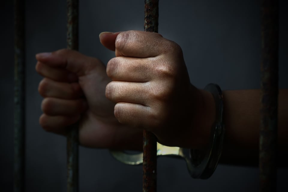 Manos de persona detenida sosteniendo barrotes de celda